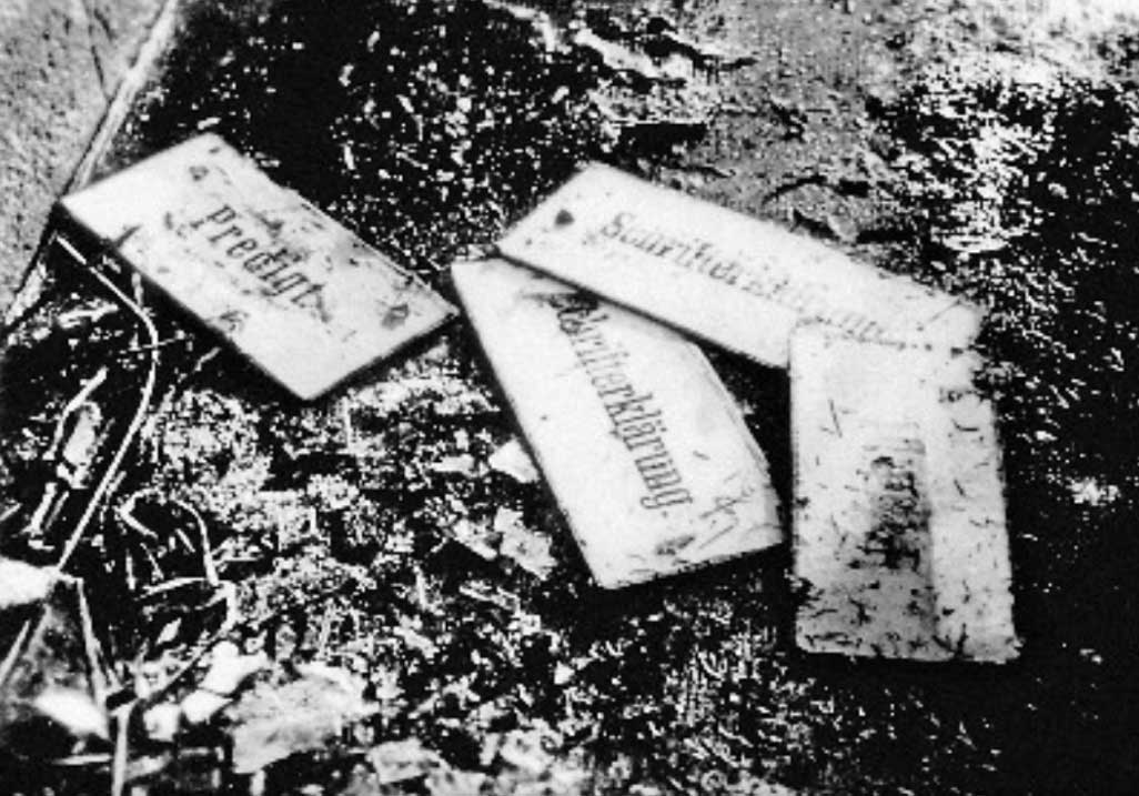 Abgenutzte Namensschilder liegen auf einem schmutzigen Boden, umgeben von unklaren Gegenständen.