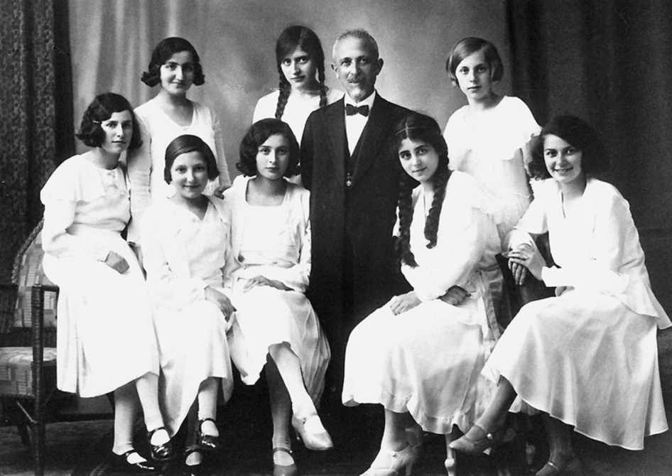 Historisches Schwarz-Weiß-Foto einer Gruppe Frauen in weißen Kleidern mit einem Mann im Anzug und Fliege.