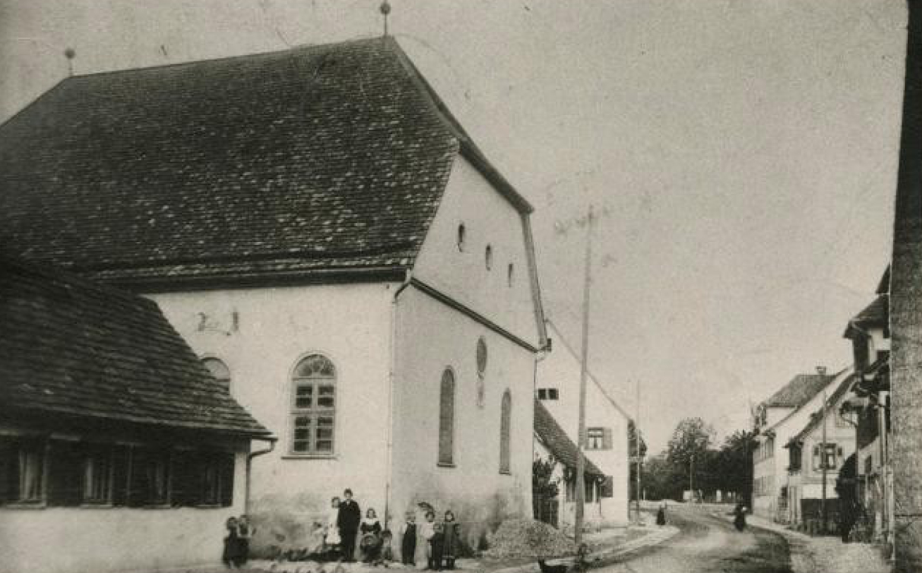 Historisches Schwarz-Weiß-Foto einer Straße mit Kirche und Gebäuden im Hintergrund.