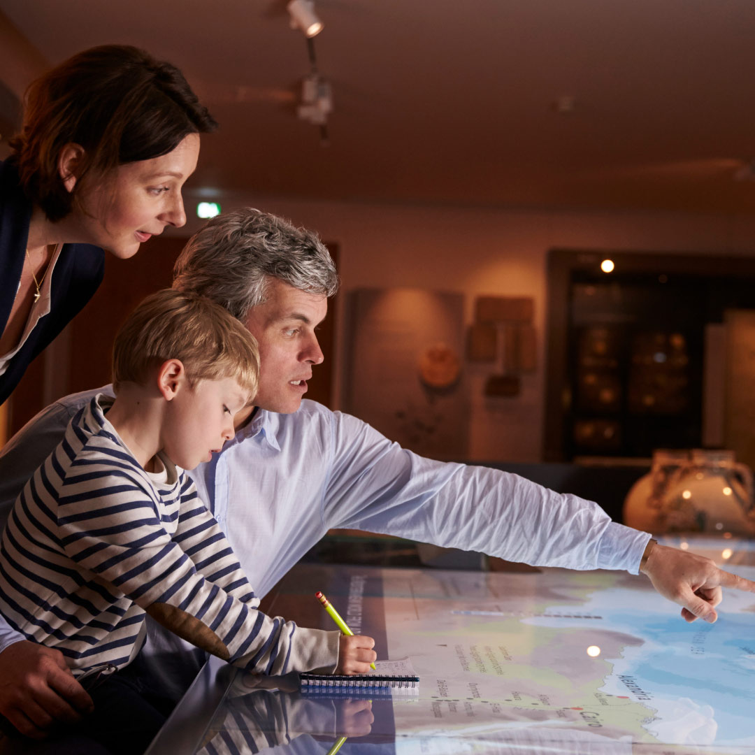 Familie erkundet interaktive Ausstellung im Museum und zeigt auf eine Karte.