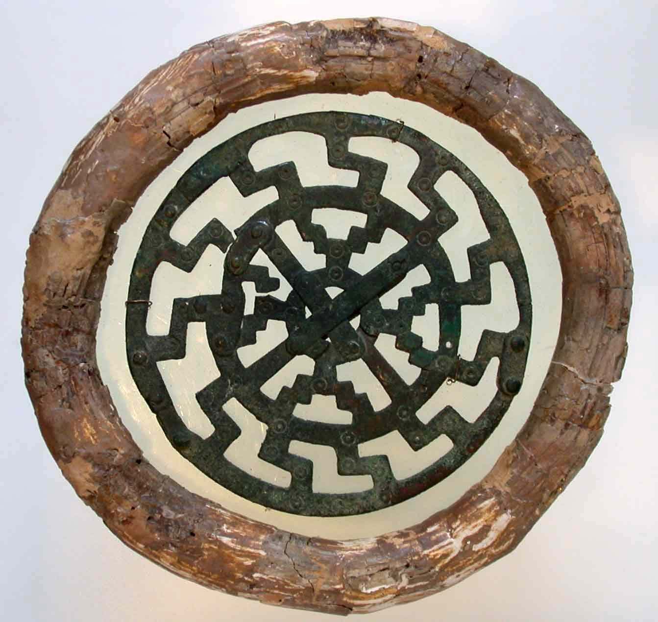 Antiker runder Mechanismus mit metallischen Zacken auf hellem Hintergrund, eingefasst in einen rustikalen Holzrahmen.