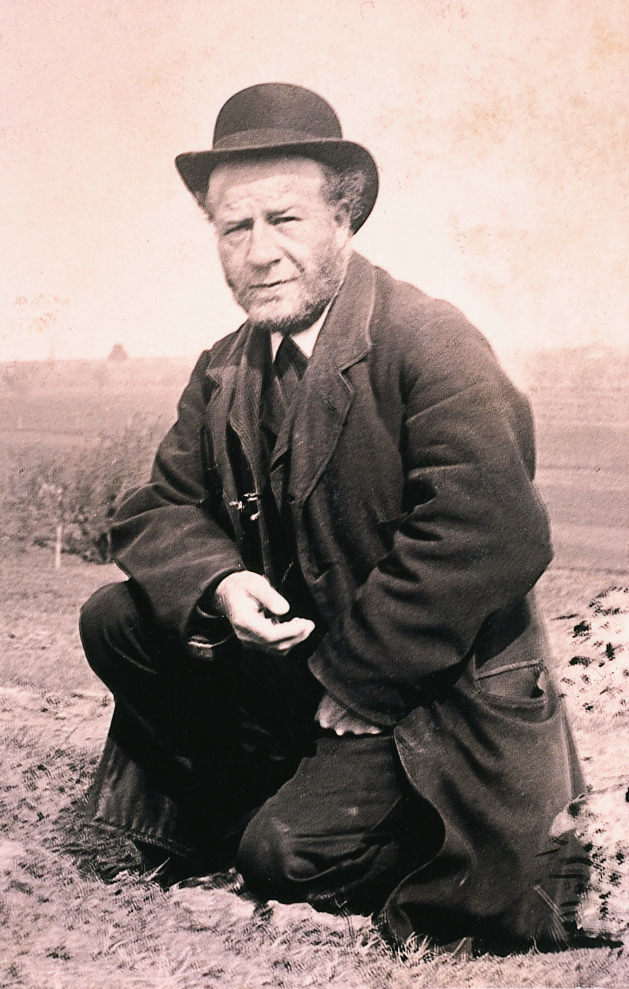Älterer Mann mit auffälligem Hut, kniend in der Natur, nachdenklicher Ausdruck, im historischen Fotostil.